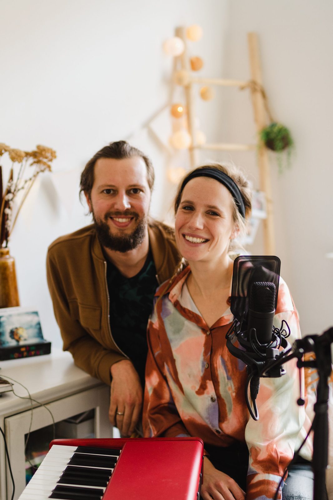Zeb en Noesjka lachend achter een rode piano en een microfoon in hun muziekkamer